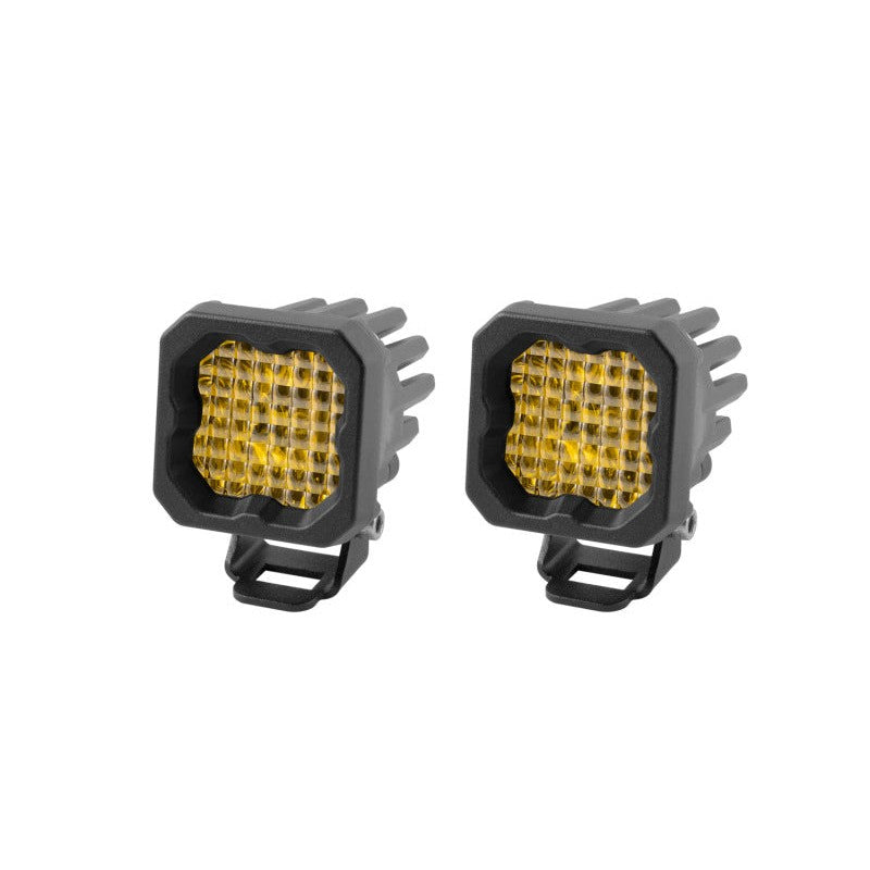Pair of compact Stage Series C1 Sport yellow LED pods with black powdercoated aluminum housings and amber backlighting.