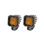 Pair of Diode Dynamics Stage Series C1 yellow LED fog pods with black powder-coated housings and amber backlighting.