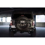 DV8 Offroad black aluminum spare tire guard and accessory mount installed on a Ford Bronco tailgate.
