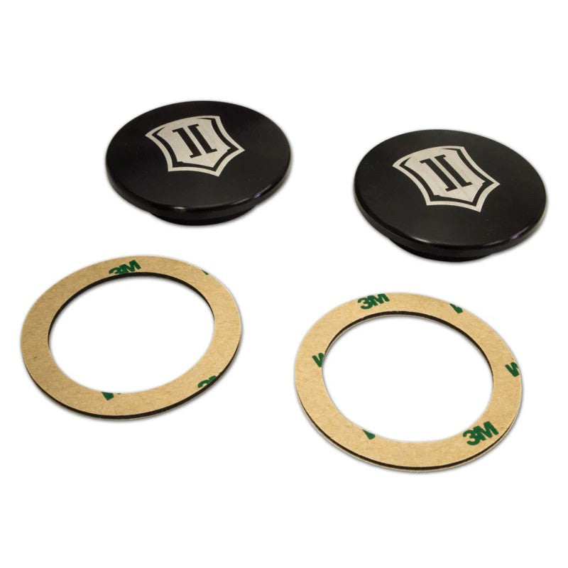 Pair of black anodized ICON billet aluminum uniball cover caps with laser-etched logos and 3M adhesive rings.
