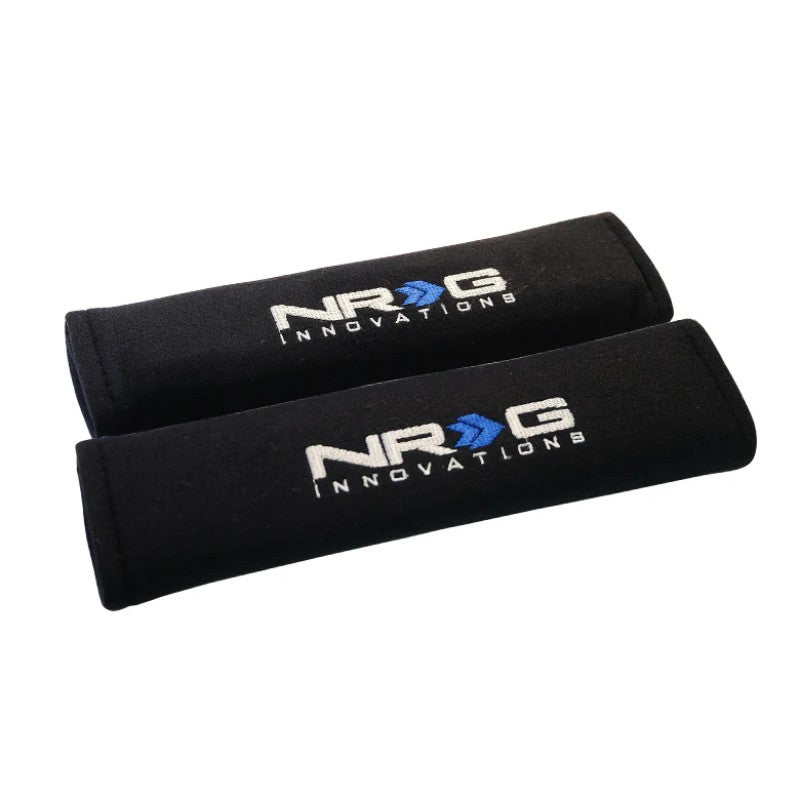 Pair of black NRG Innovations short seat belt pads, 2.7 inches wide by 11 inches long with hook-and-loop closure.