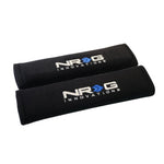 Pair of black NRG Innovations short seat belt pads, 2.7 inches wide by 11 inches long with hook-and-loop closure.