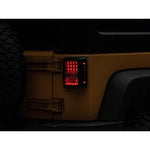 A pair of Raxiom Axial Series Lux LED tail lights for Jeep Wrangler JK with black housings and clear lenses.